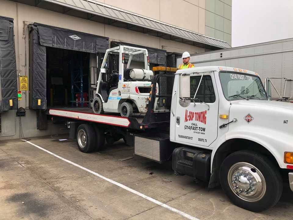 Man in a baseball cap inspecting the open hood of a gray semi-truck in a parking lot.