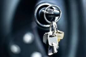 Mechanic in blue overalls walks toward a broken-down car, family looking at open hood.