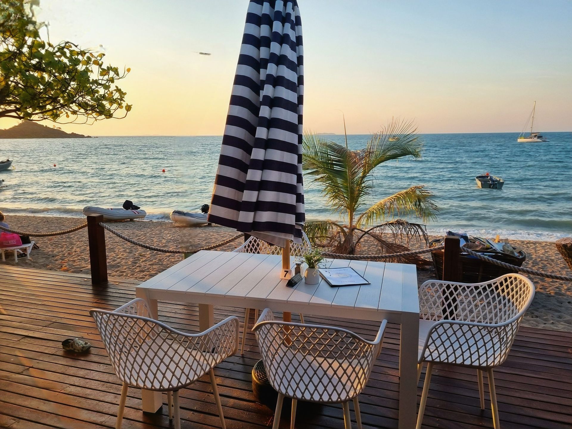 Beachside Table Setting With Striped Umbrella and Chairs — The Beach Bar and Restaurant at Montes in Cape Gloucester, QLD
