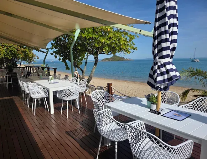Outdoor beachside restaurant with white tables and chairs — The Beach Bar and Restaurant at Montes in Cape Gloucester, QLD