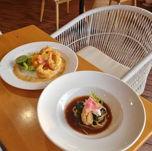 Two plates of food on a table near a white woven chair — The Beach Bar and Restaurant at Montes in Cape Gloucester, QLD