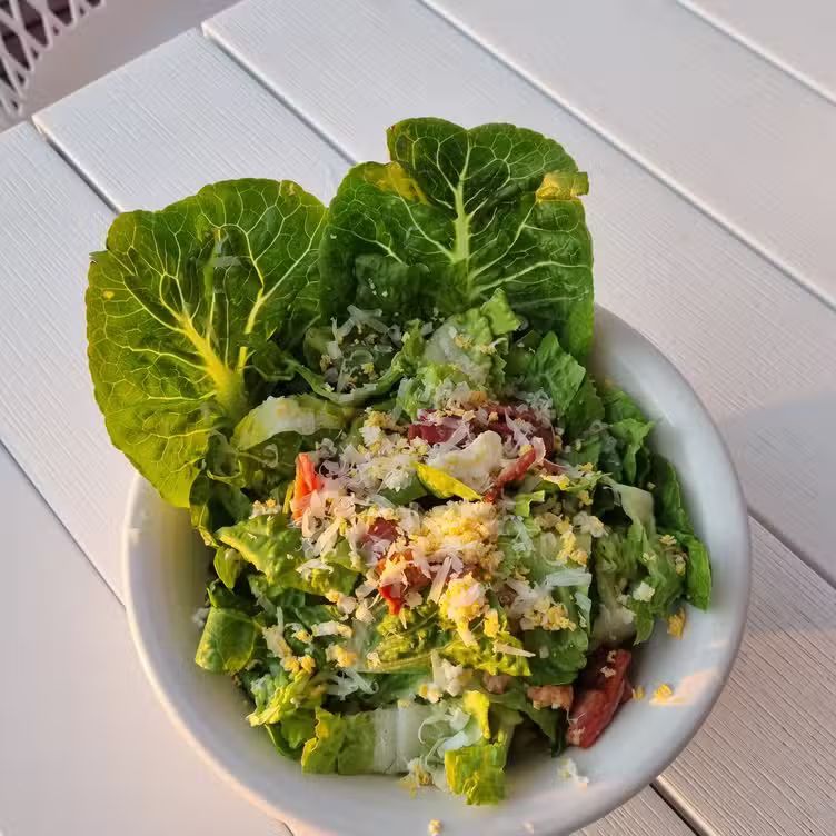 Caesar salad in a white bowl on a white wooden table — The Beach Bar and Restaurant at Montes in Cape Gloucester, QLD