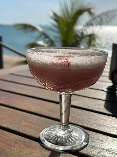 Pink cocktail in a stemmed glass on a wooden table — The Beach Bar and Restaurant at Montes in Cape Gloucester, QLD
