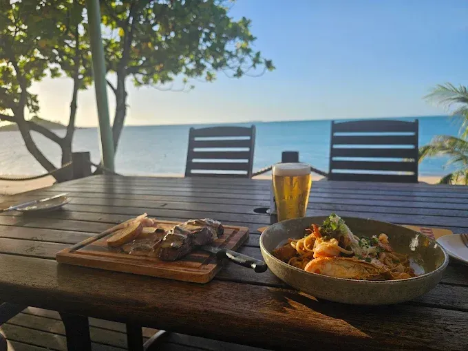 Wooden table with steak, pasta and beer — The Beach Bar and Restaurant at Montes in Cape Gloucester, QLD