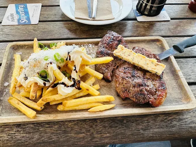 Steak with fries, cheese, and a sauce on a wooden tray — The Beach Bar and Restaurant at Montes in Cape Gloucester, QLD