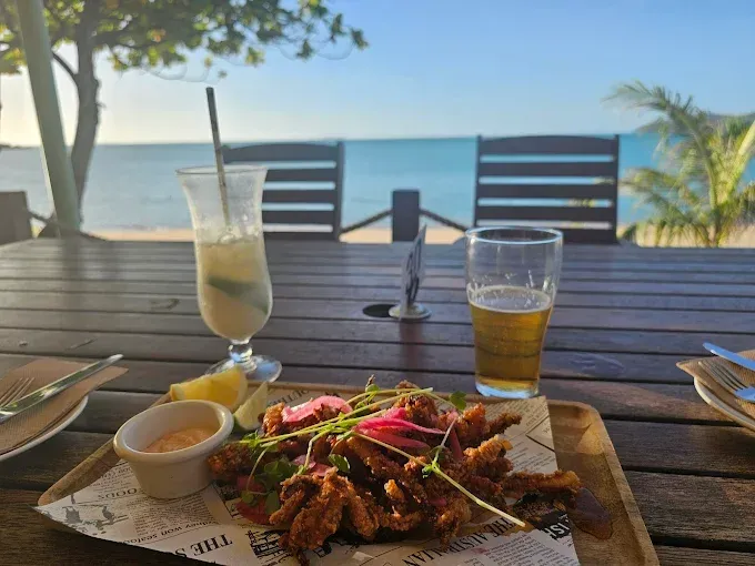 Fried food platter, cocktail, and beer on a wooden table — The Beach Bar and Restaurant at Montes in Cape Gloucester, QLD