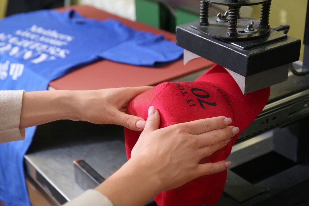 Two Hands Position a Red Fabric Under a Heat Press Machine — DXMA Designs In Nowra, NSW