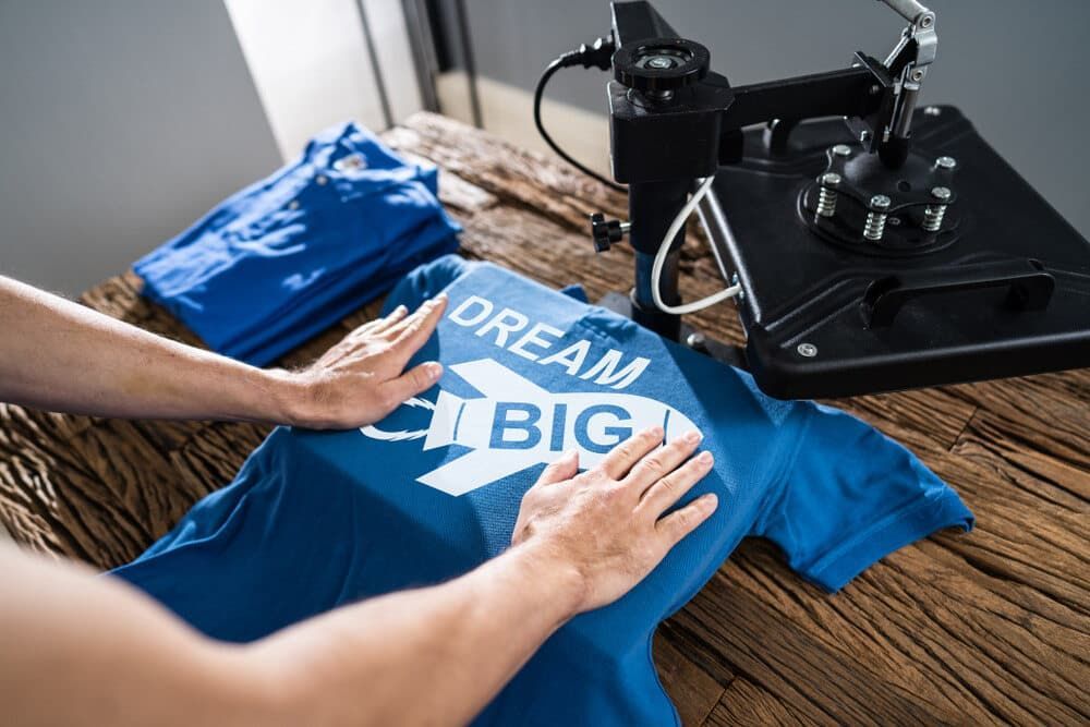 Person Applying Decal on a Blue T-shirt Using a Heat Press Machine — DXMA Designs In Nowra, NSW