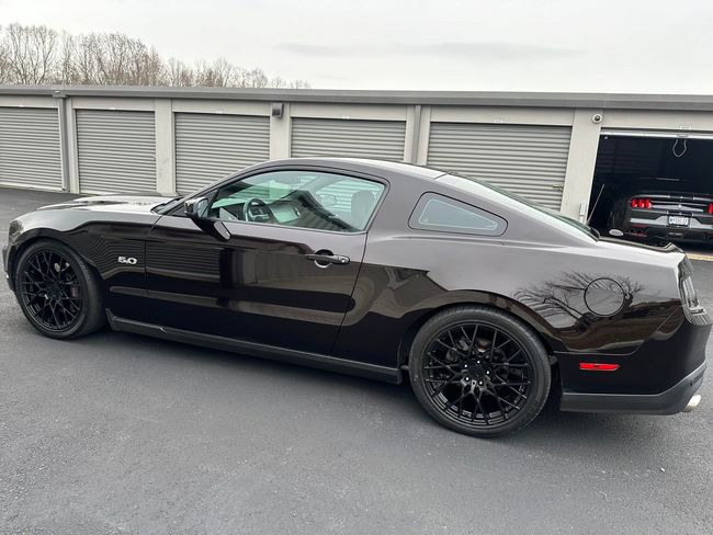 Black Ford Mustang with black rims parked in front of storage units.