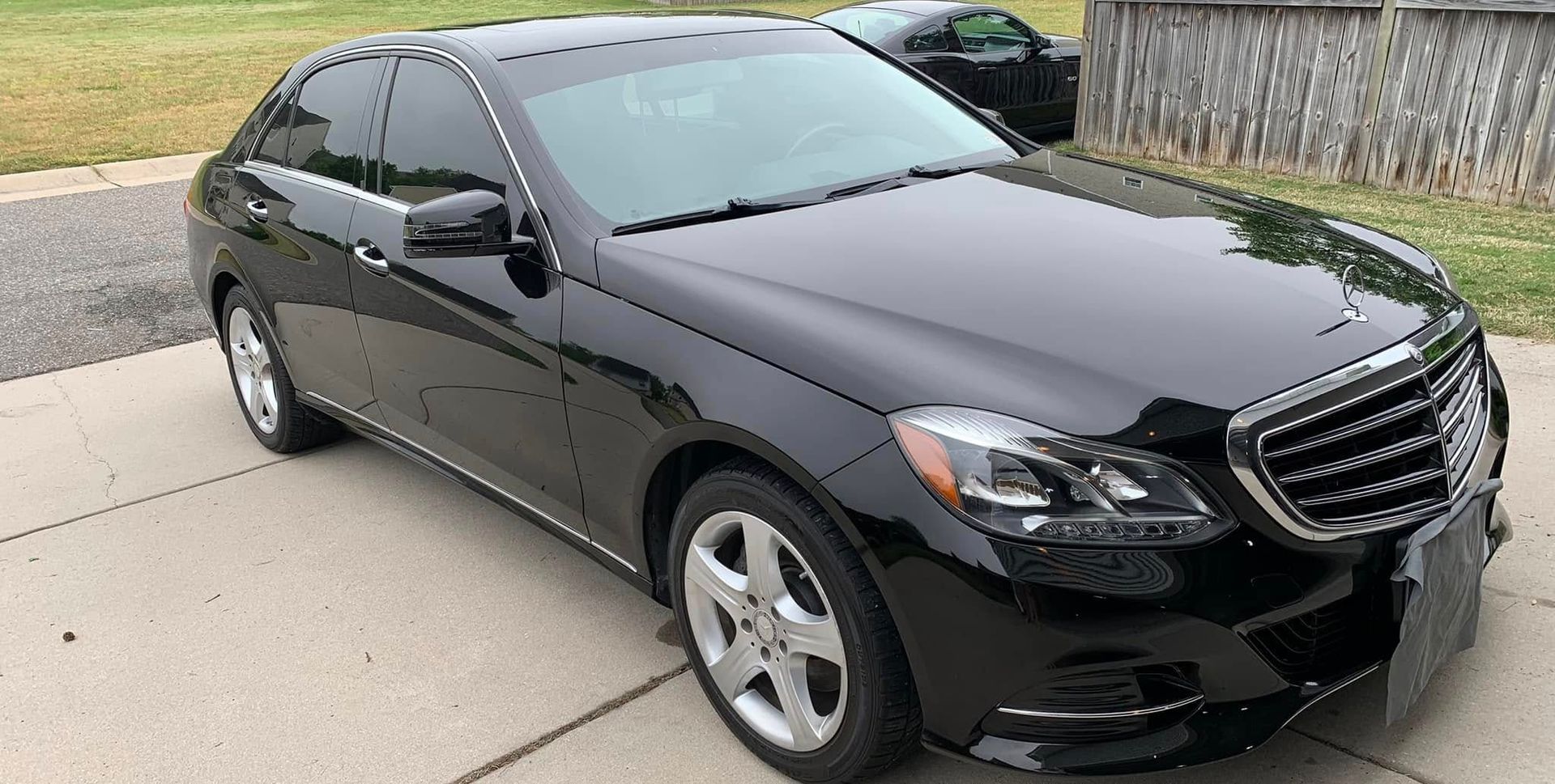 Black Mercedes-Benz sedan parked on a driveway with tinted windows, parked next to a lawn.