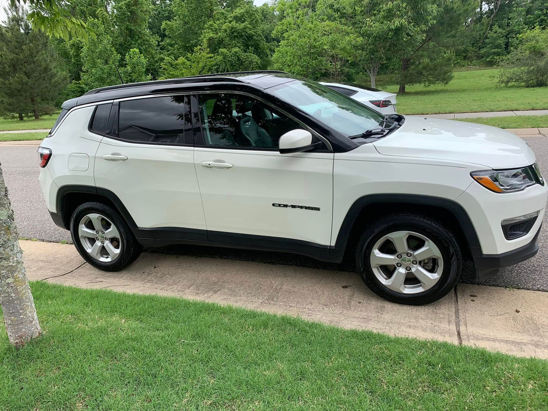 White Jeep Compass parked on a sidewalk next to grass. Black roof and trim.