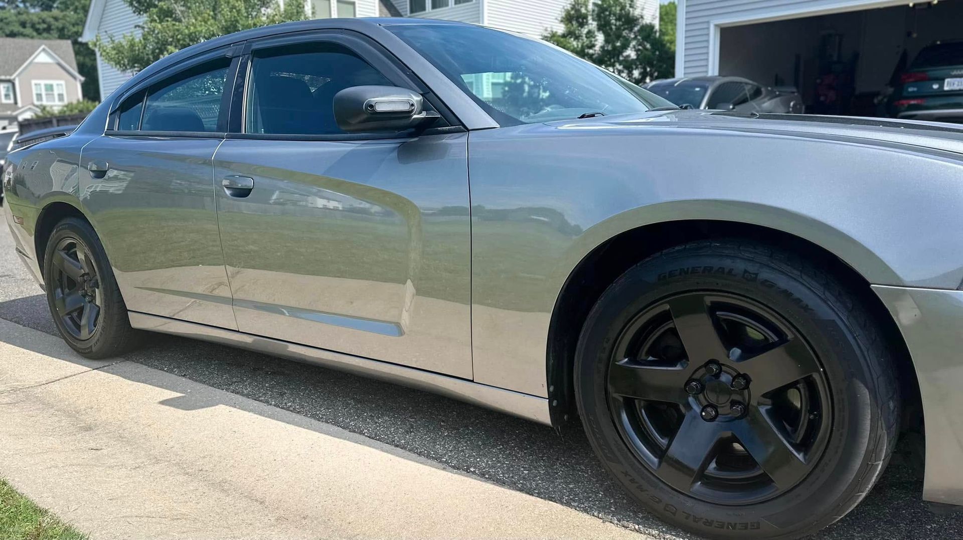 Silver Dodge Charger with black wheels and tinted windows parked on a driveway.