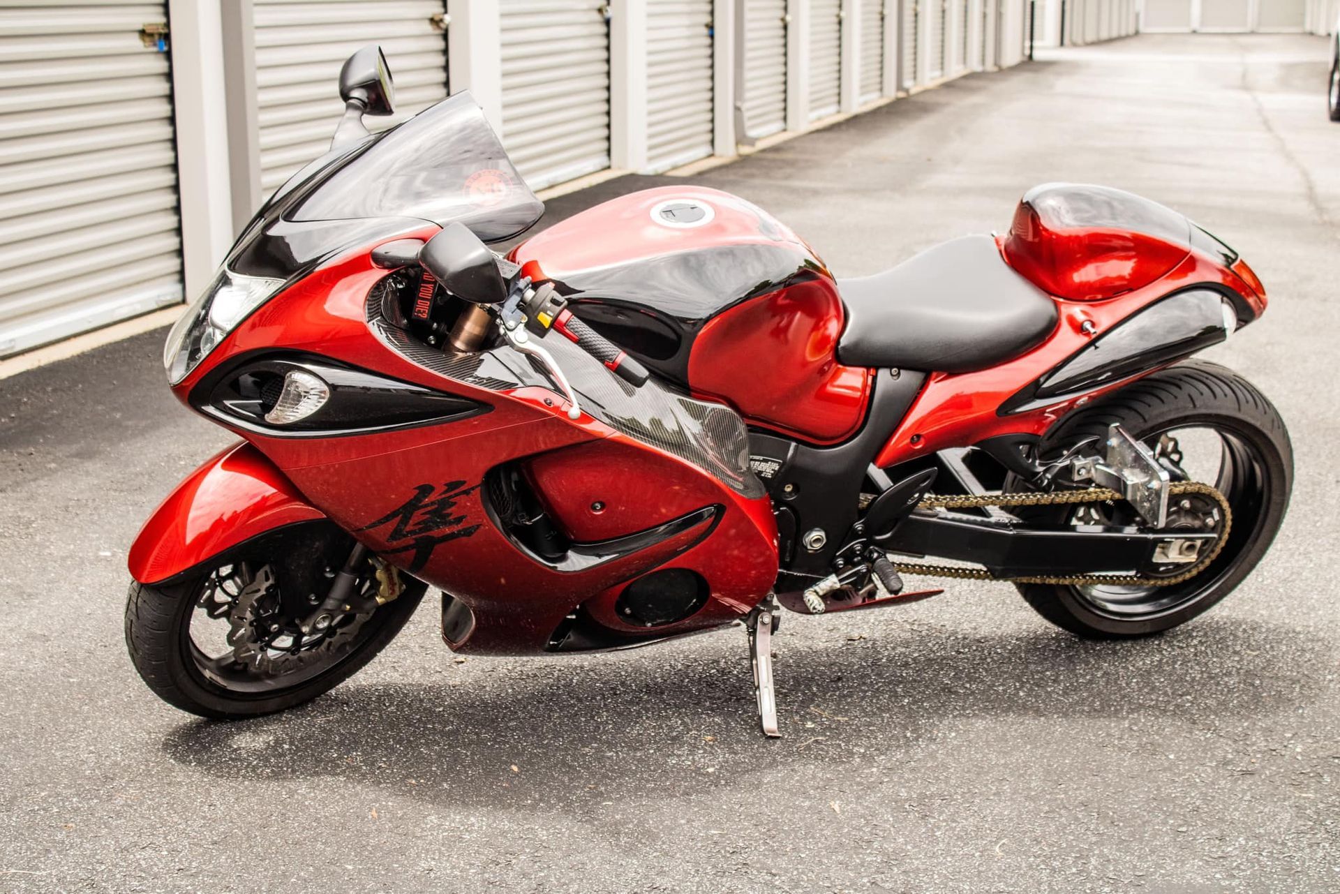 Red and black Suzuki Hayabusa motorcycle parked on wet pavement in front of storage units.