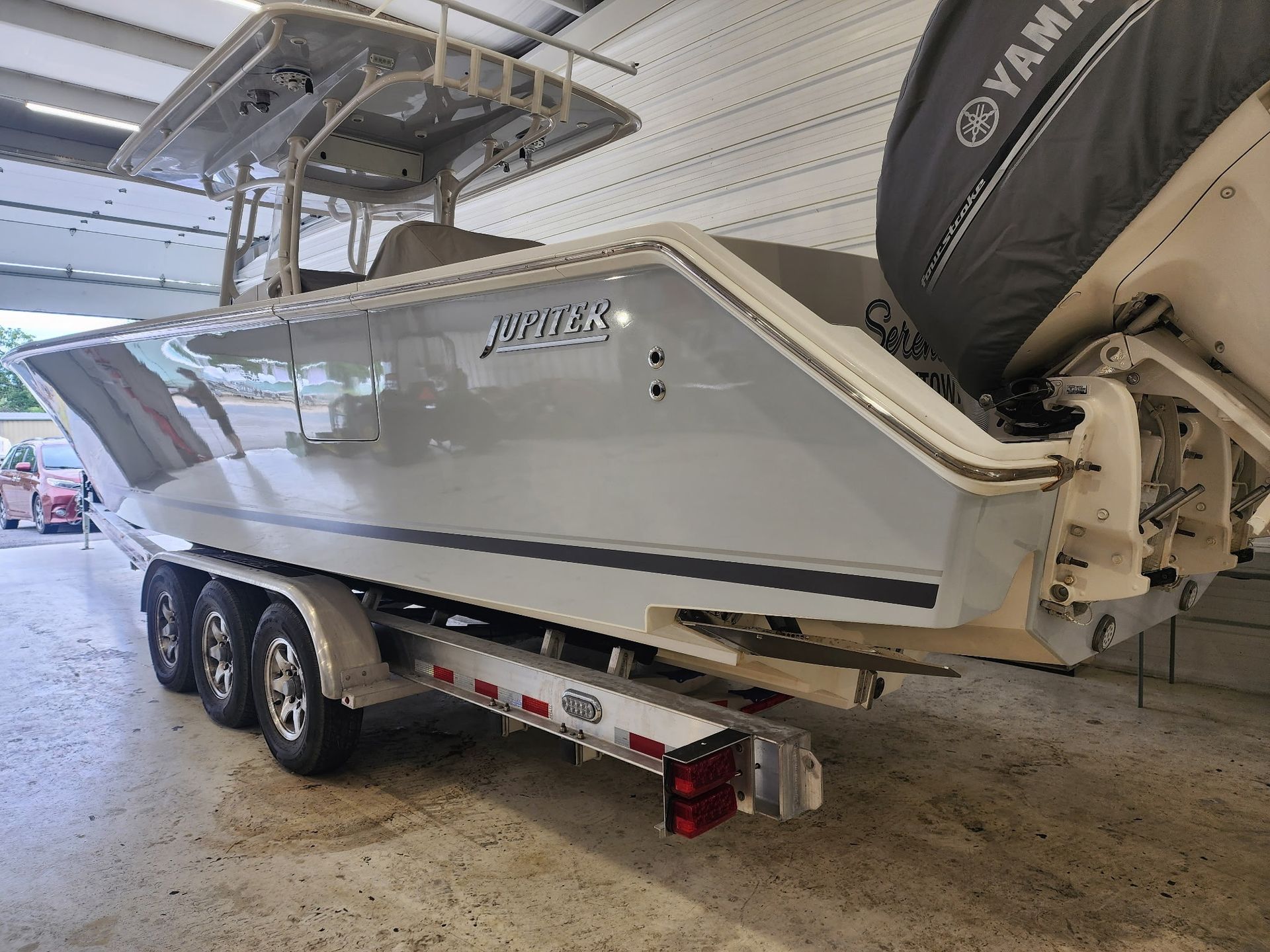 A light gray Jupiter boat on a trailer, with a Yamaha engine, in a garage.