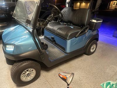 Blue golf cart with black seats, golf club in foreground.