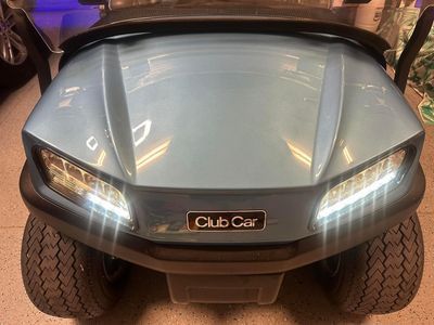 Light blue Club Car golf cart with bright headlights.