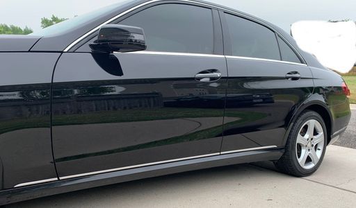 Black Mercedes sedan parked on a paved driveway with tinted windows.