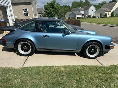 Blue Porsche 911 Targa parked on a driveway with black accents and white wheels, houses in background.
