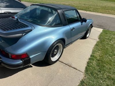 Blue Porsche Targa parked on a driveway with black roof and white-rimmed wheels.