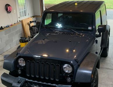 Dark gray Jeep Wrangler parked inside a garage; visible from the front, with a window and cleaning supplies in the background.