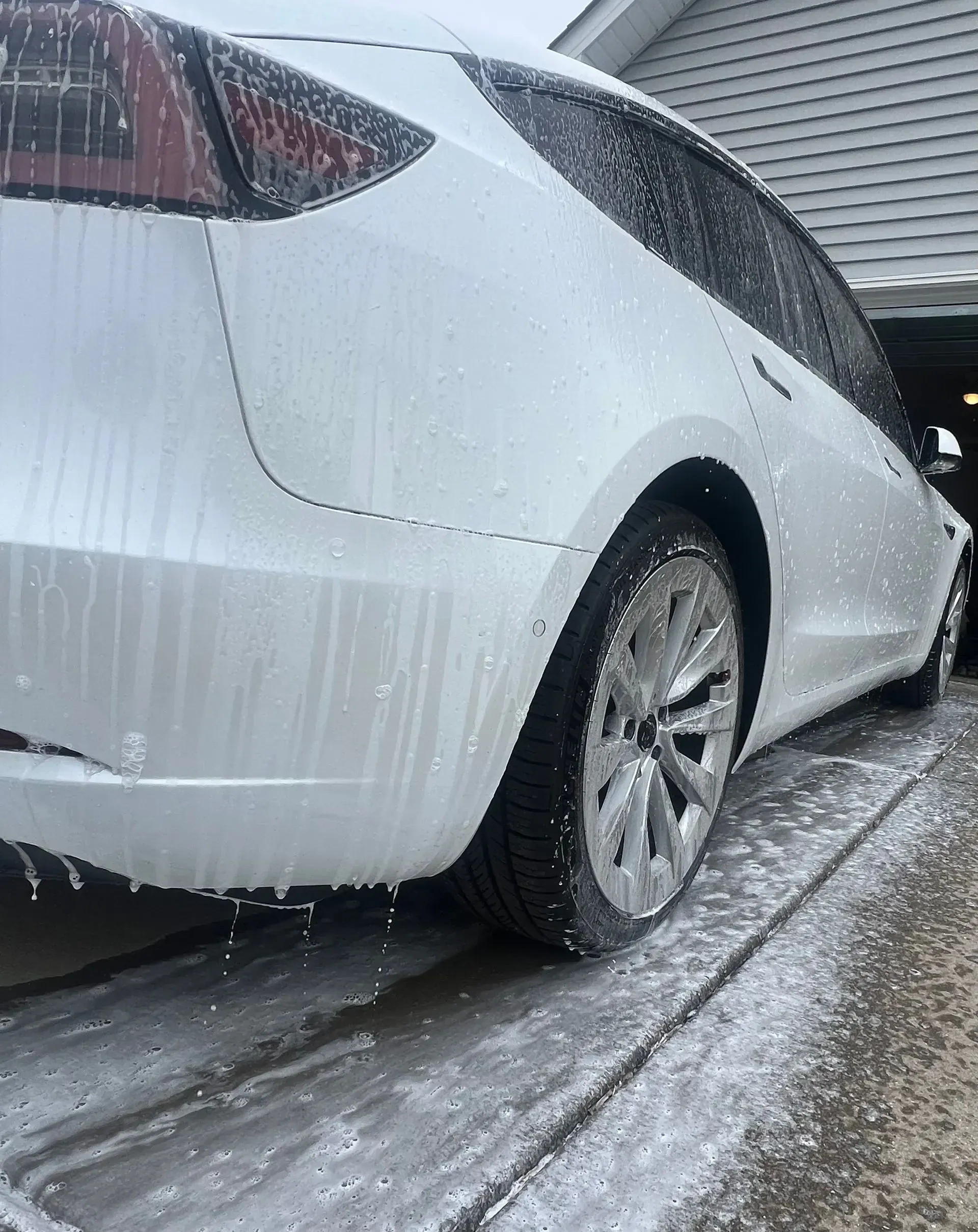White Tesla car being washed with foamy soap in a driveway.