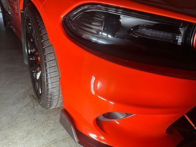 Red car's front end. Black tire, headlight, and bumper.