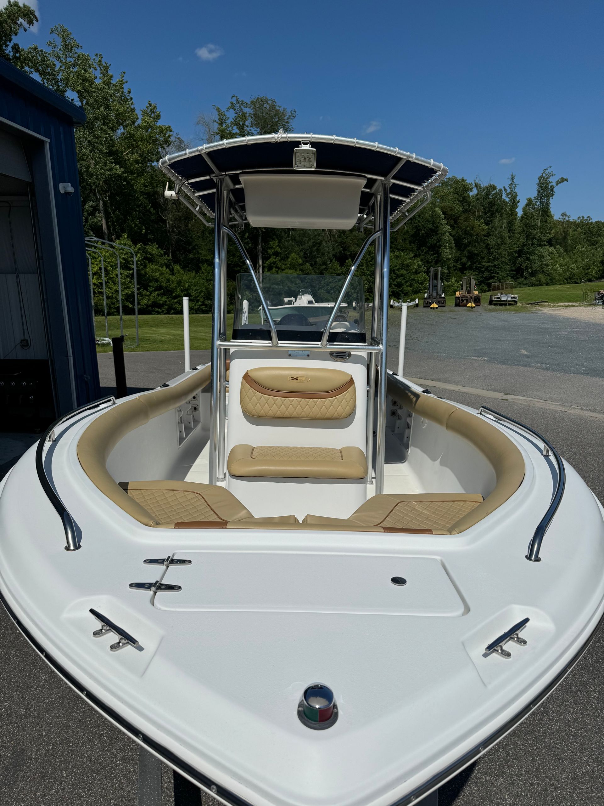 White boat with tan interior, blue canopy. Outdoors on a sunny day.
