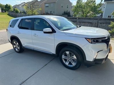 White SUV parked on a concrete driveway, in front of a house with green lawn, in a neighborhood.