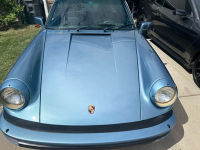 Blue Porsche 911, front view, with round headlights. Parked on a driveway, sunny day.