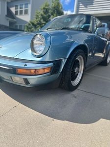 Blue Porsche 911 parked on a driveway, featuring a round headlight and black and white rims.