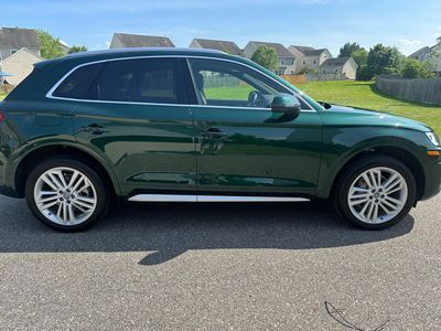 Green Audi Q5 SUV parked on a paved road, houses and lawn in the background.