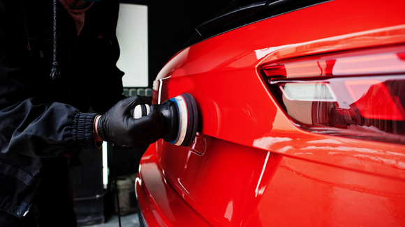 Person polishing a red car with a black polishing tool.