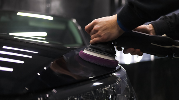 Hands using a polisher on a black car to refine its paint.