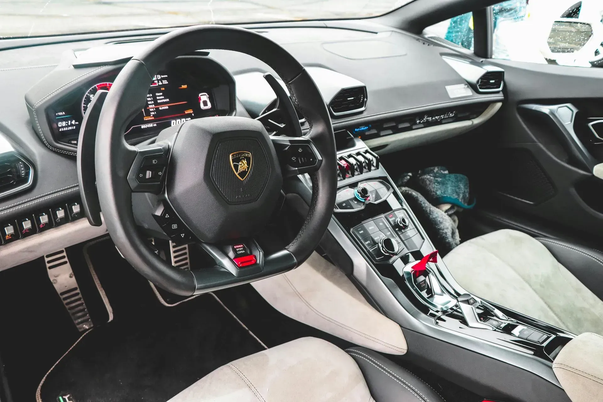 Interior of a Lamborghini Huracán. Black and gray dashboard, steering wheel with gold emblem, light-colored seats.