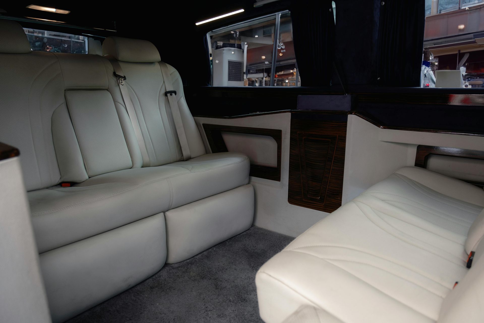 Interior of a limousine with white leather seats, dark trim, and a window.