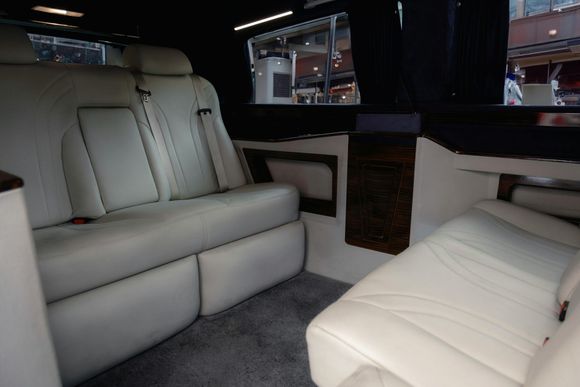 Interior of a limousine with white leather seats, dark trim, and a window.