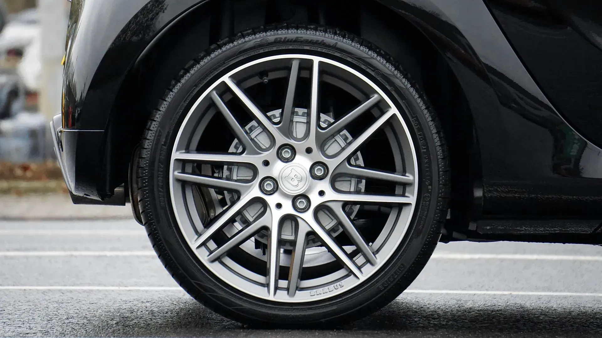Black car wheel with silver spokes, on an asphalt road.