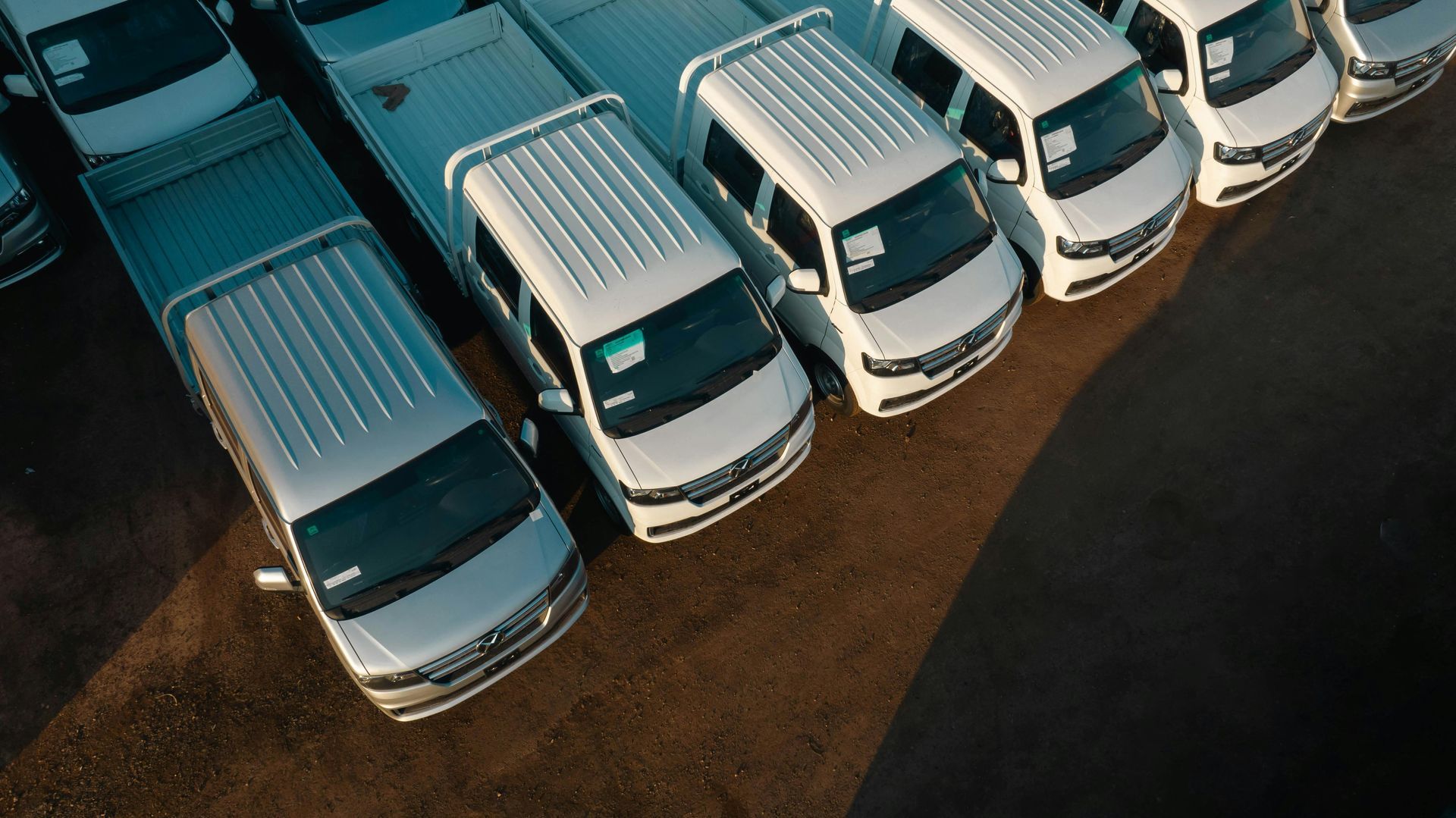 Overhead view of a row of white vans parked on a brown surface, possibly a lot.