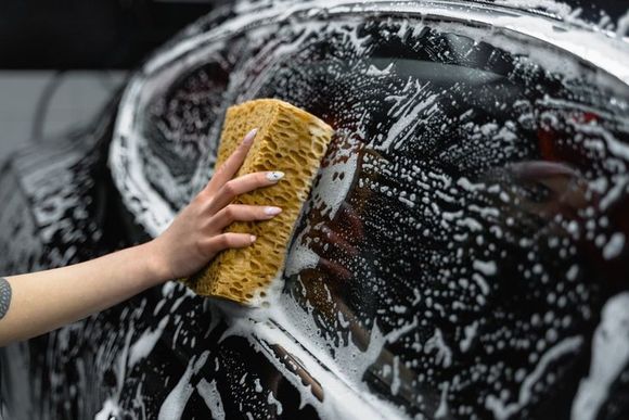 Person washing a black car with a soapy sponge.