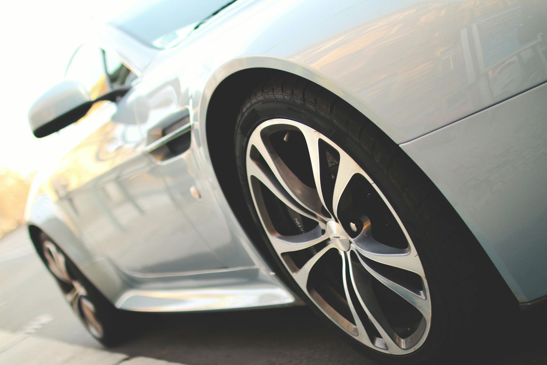 Silver luxury car, low angle view. Detailed wheel with black and silver spokes.