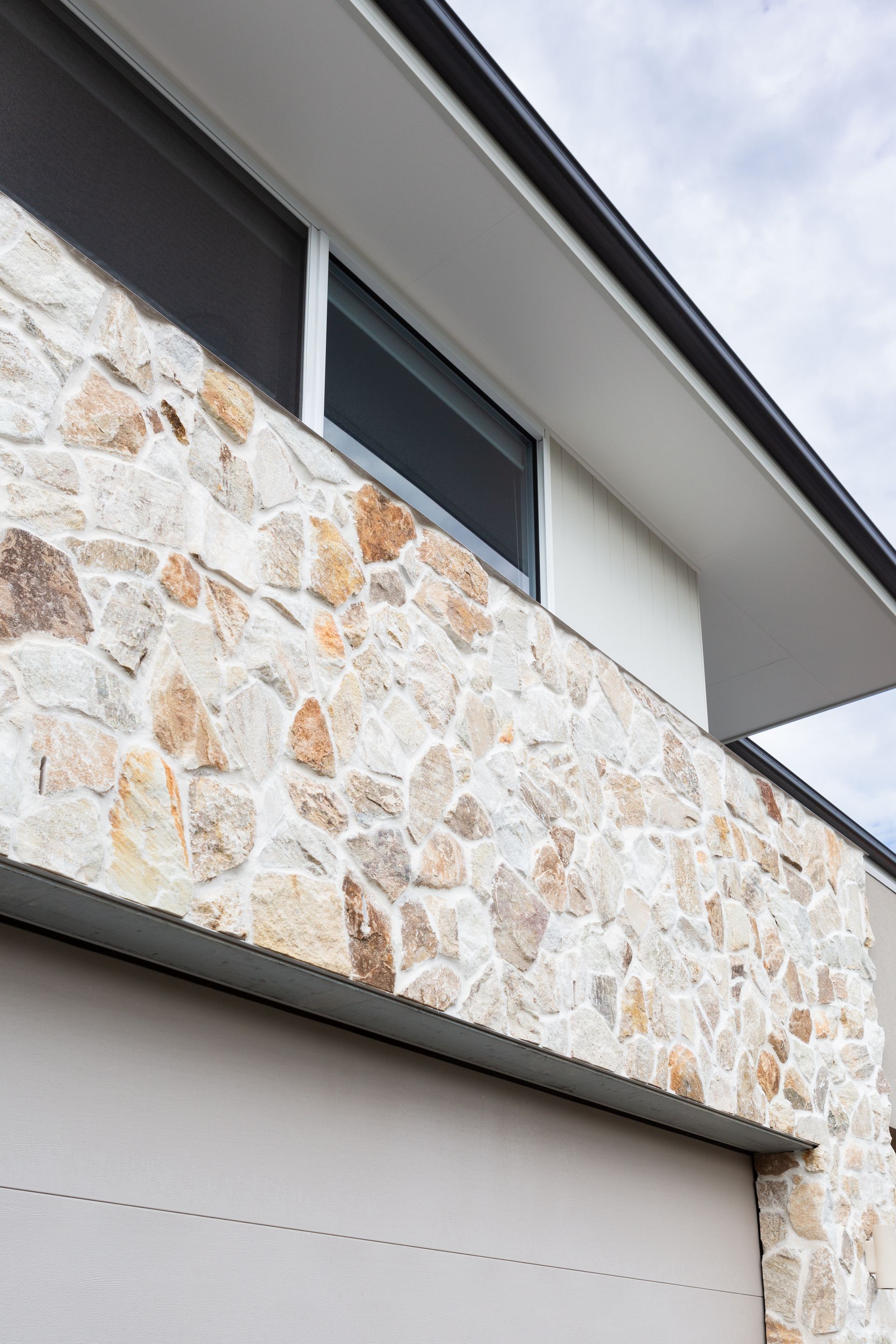 Stone exterior wall with window, light gray door, and white roof.
