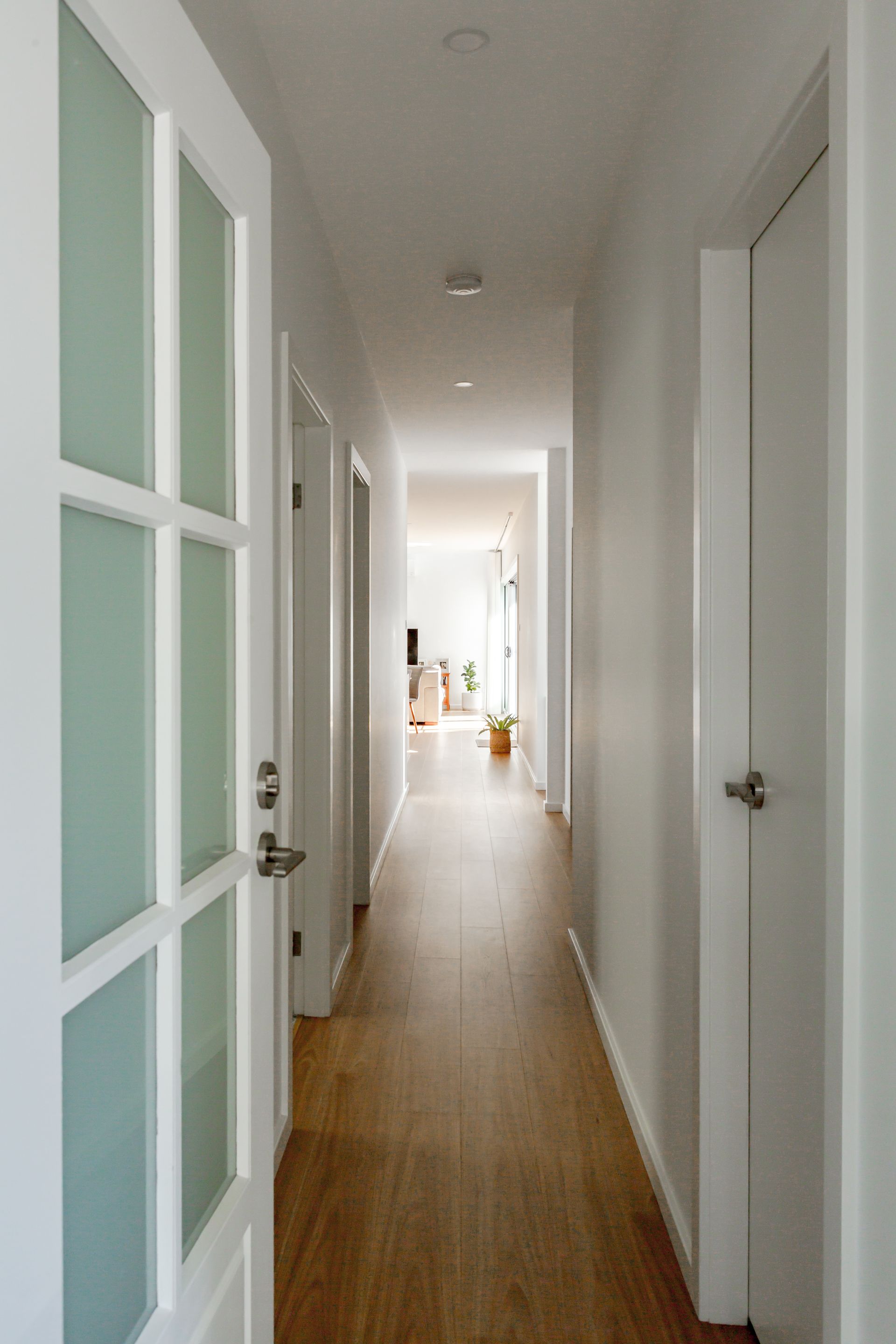 Hallway with wooden floor, white walls, and doors. Frosted glass door on the left.