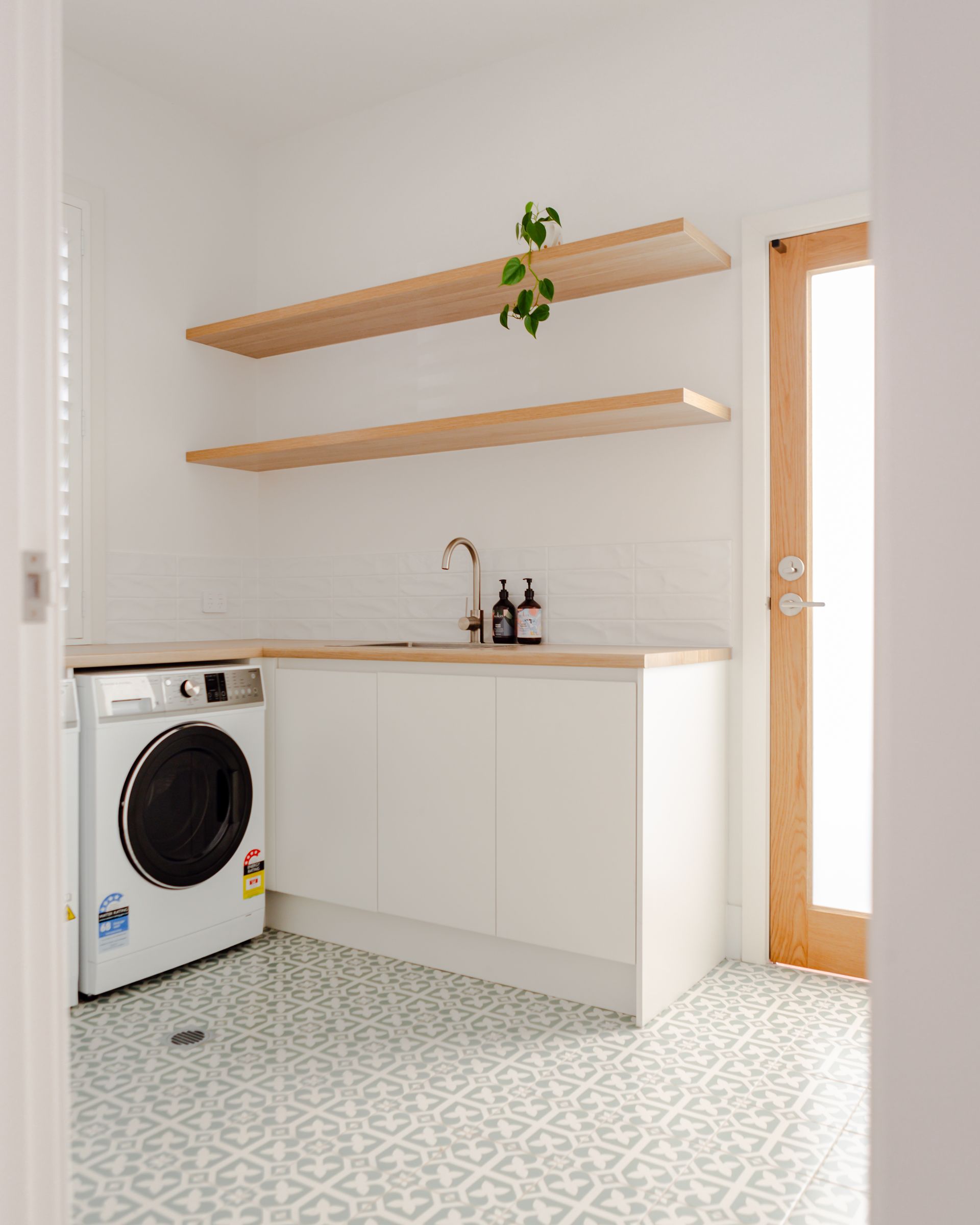 Laundry room with white cabinets, wood shelves, patterned tile, and a washing machine.
