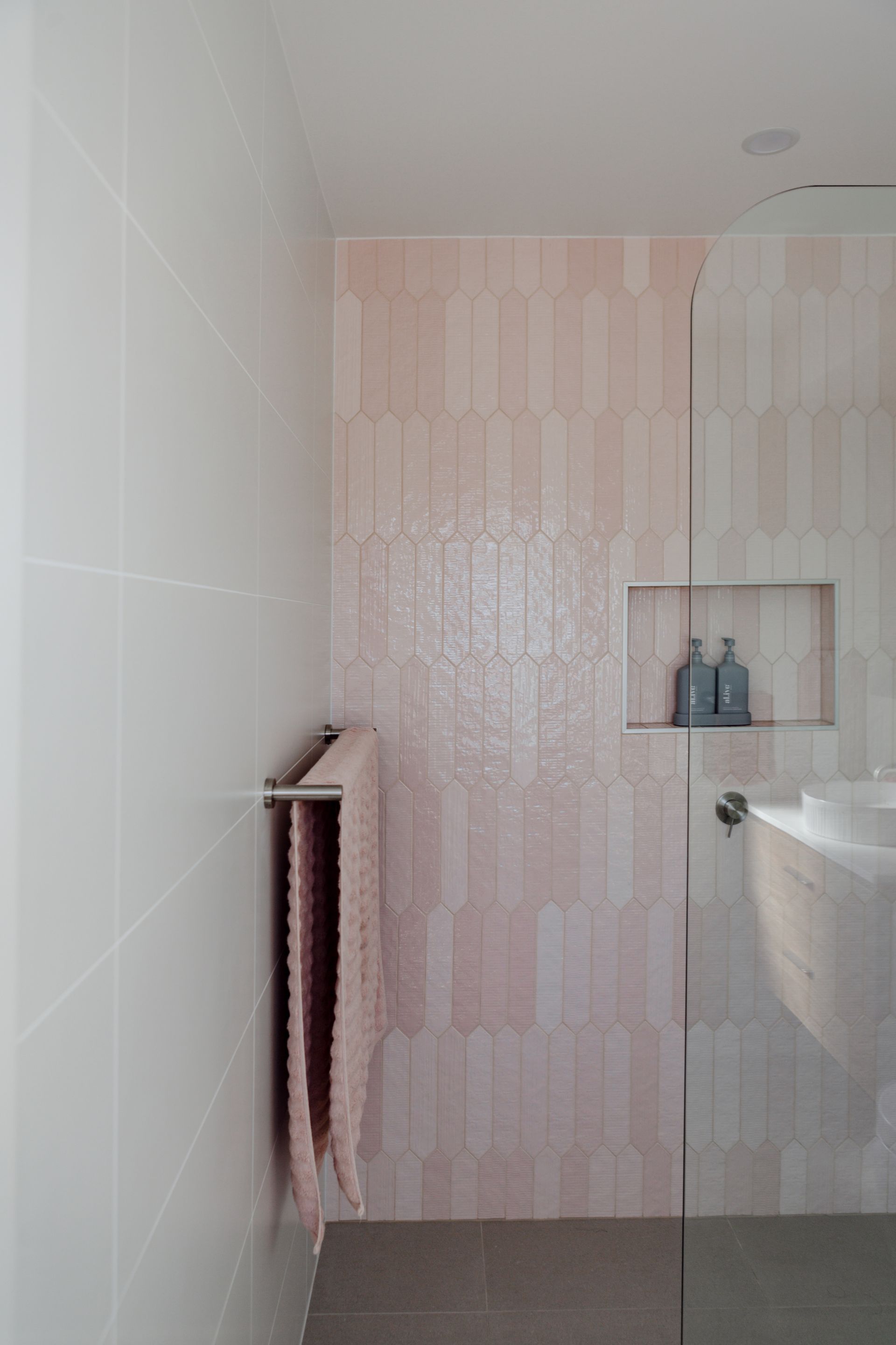 Pink and white tiled bathroom with a glass shower, towels, and built-in shelving.
