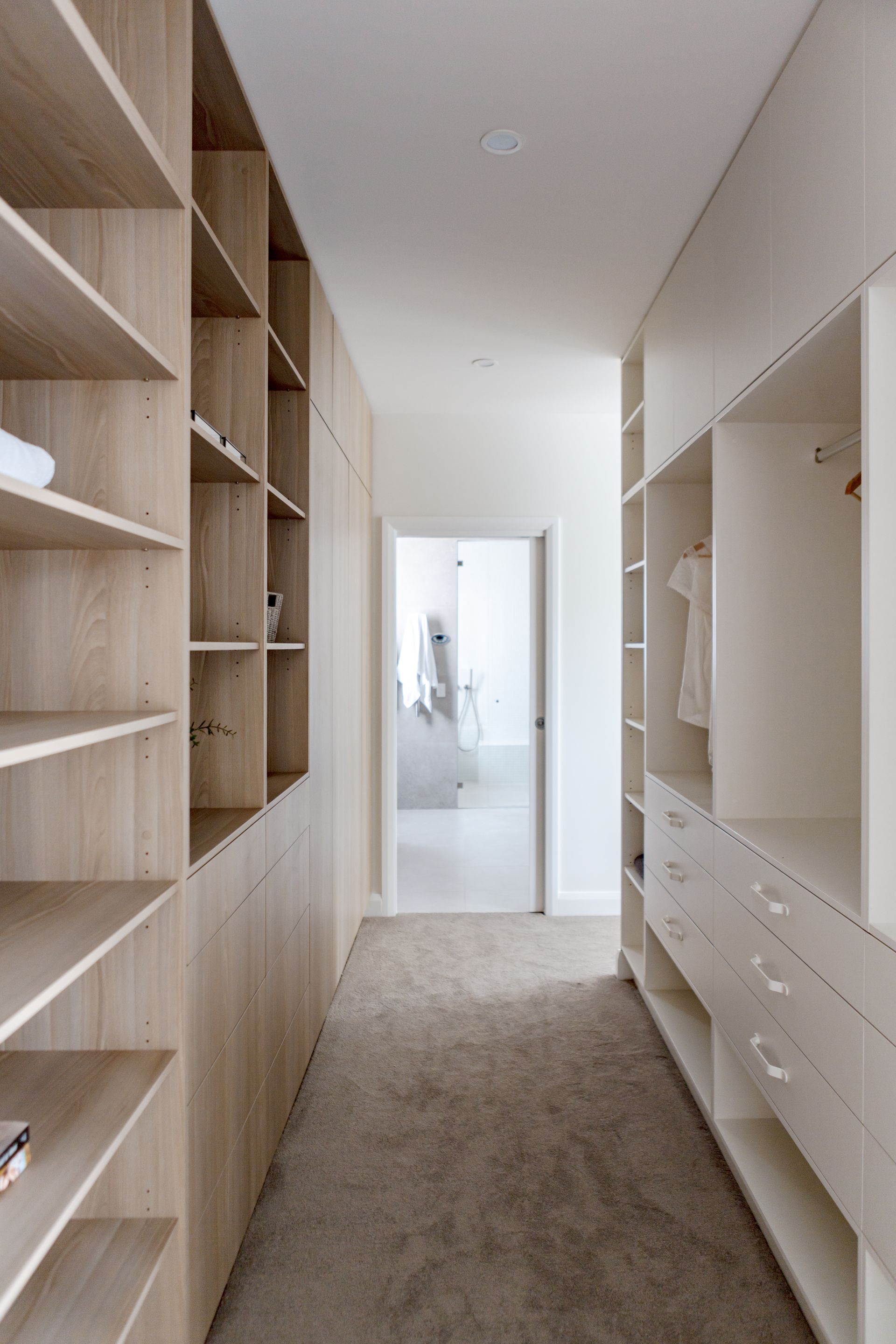 Walk-in closet with light wood shelving on one side and white cabinetry on the other, leading to a bright doorway.