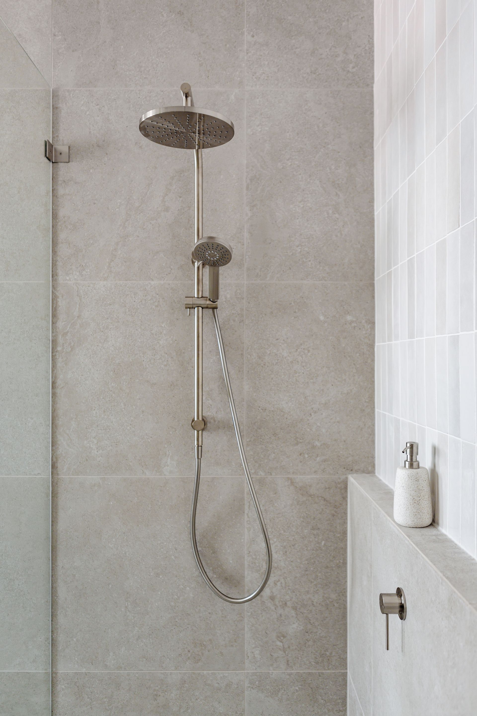 Gray tiled shower with rain shower head and hand shower.