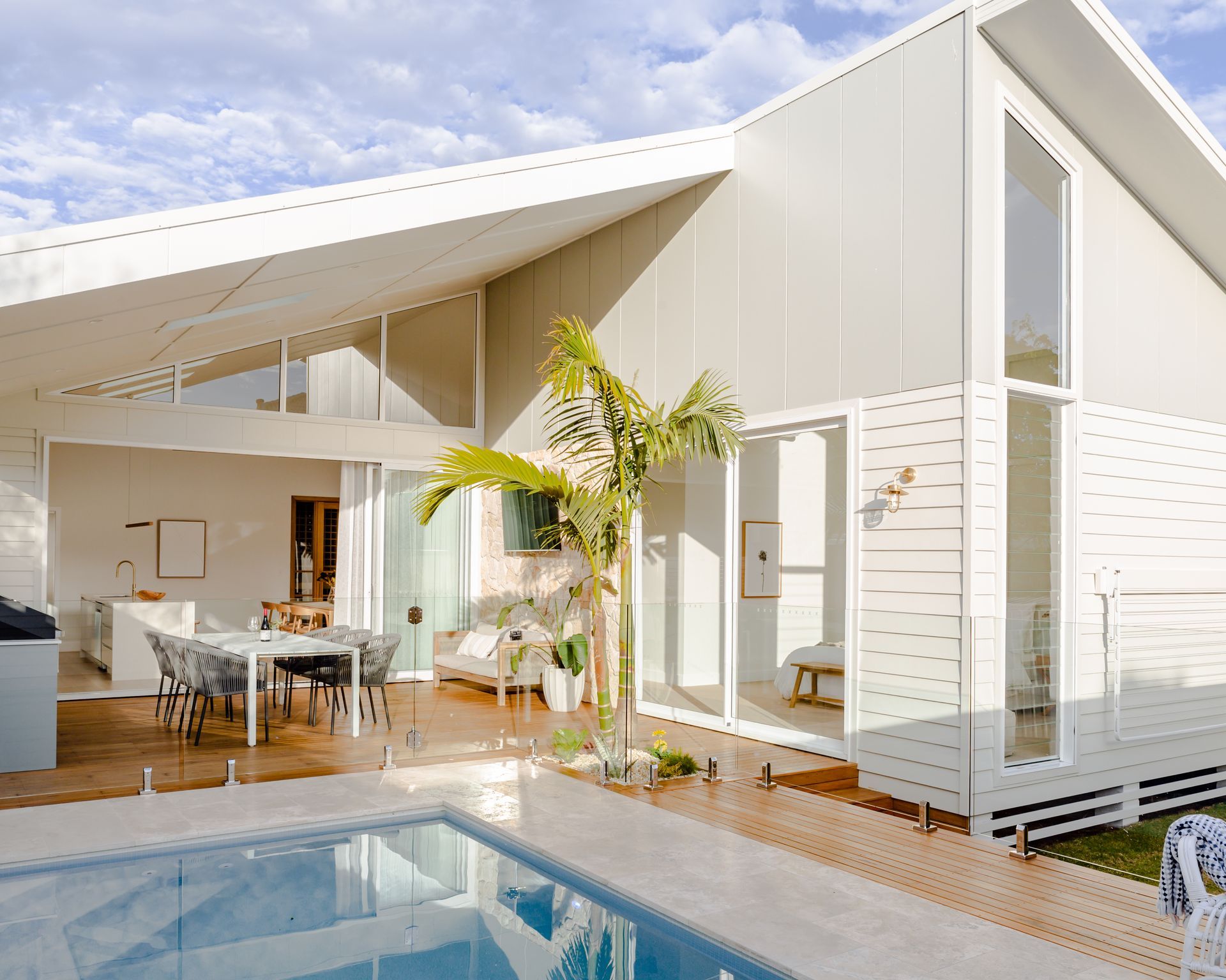 Modern house with a pool and open-air dining. White siding, large windows, and a palm tree.