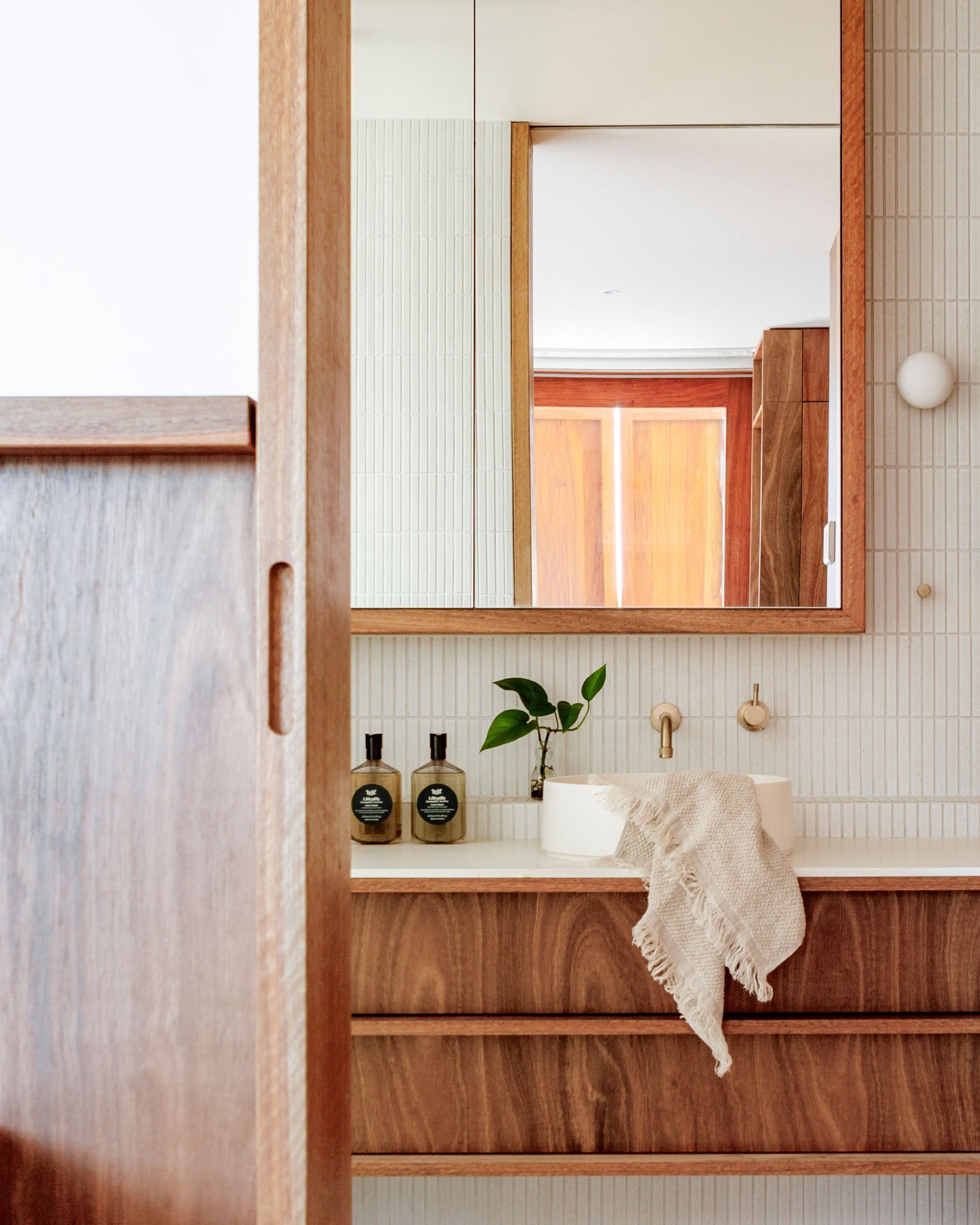 Bathroom with wooden vanity and mirror, white tile, and beige washcloth.