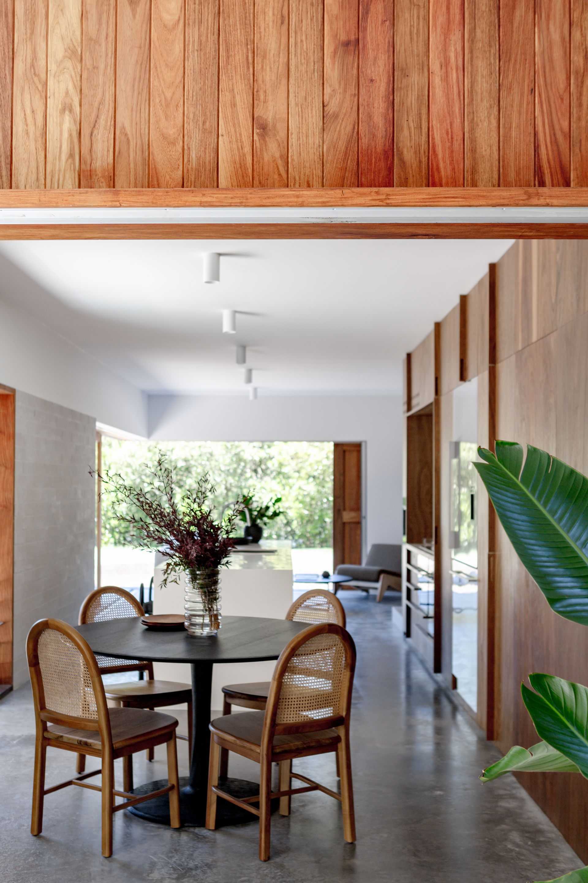 Dining room with round table and rattan chairs, light wood paneling, and natural light.