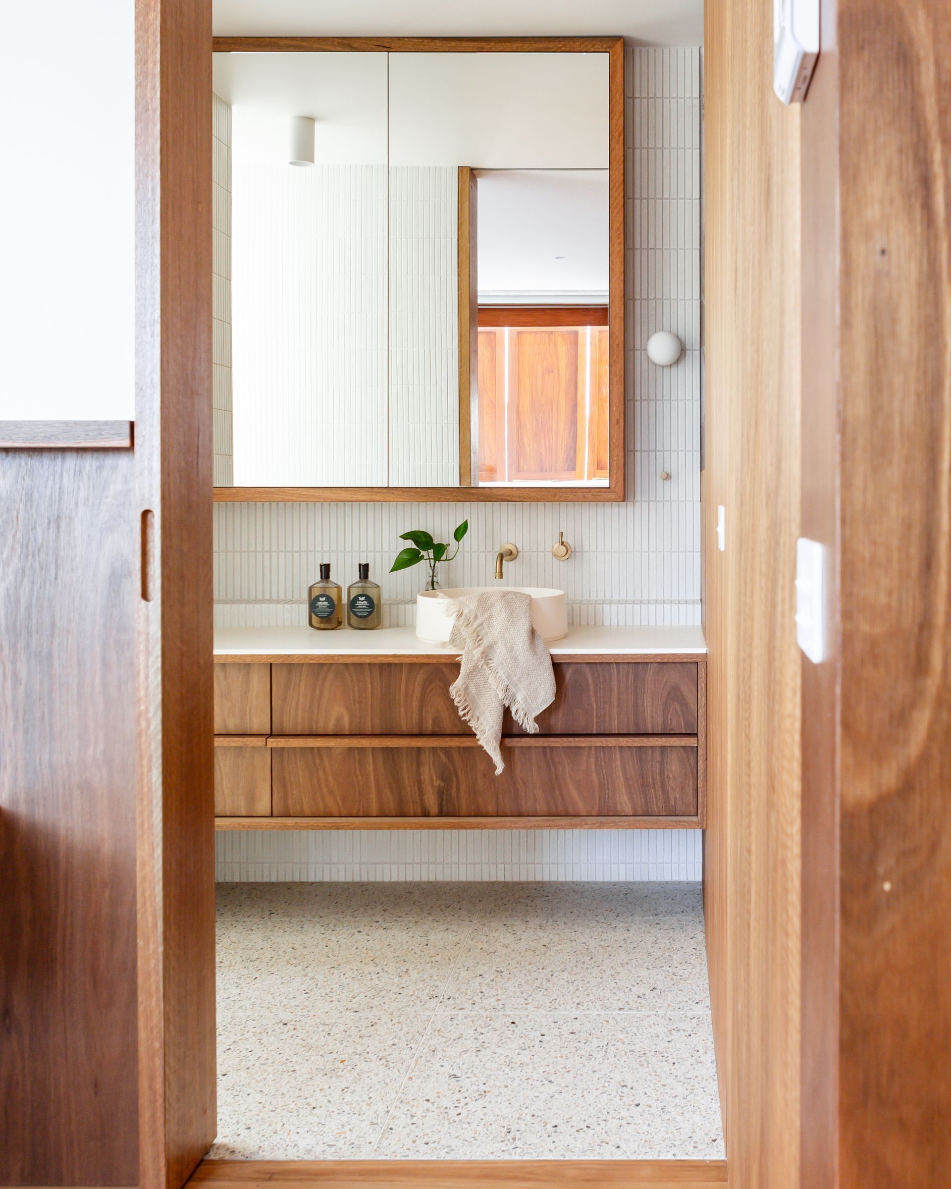 Bathroom with wood vanity, large mirror, and terrazzo floor.